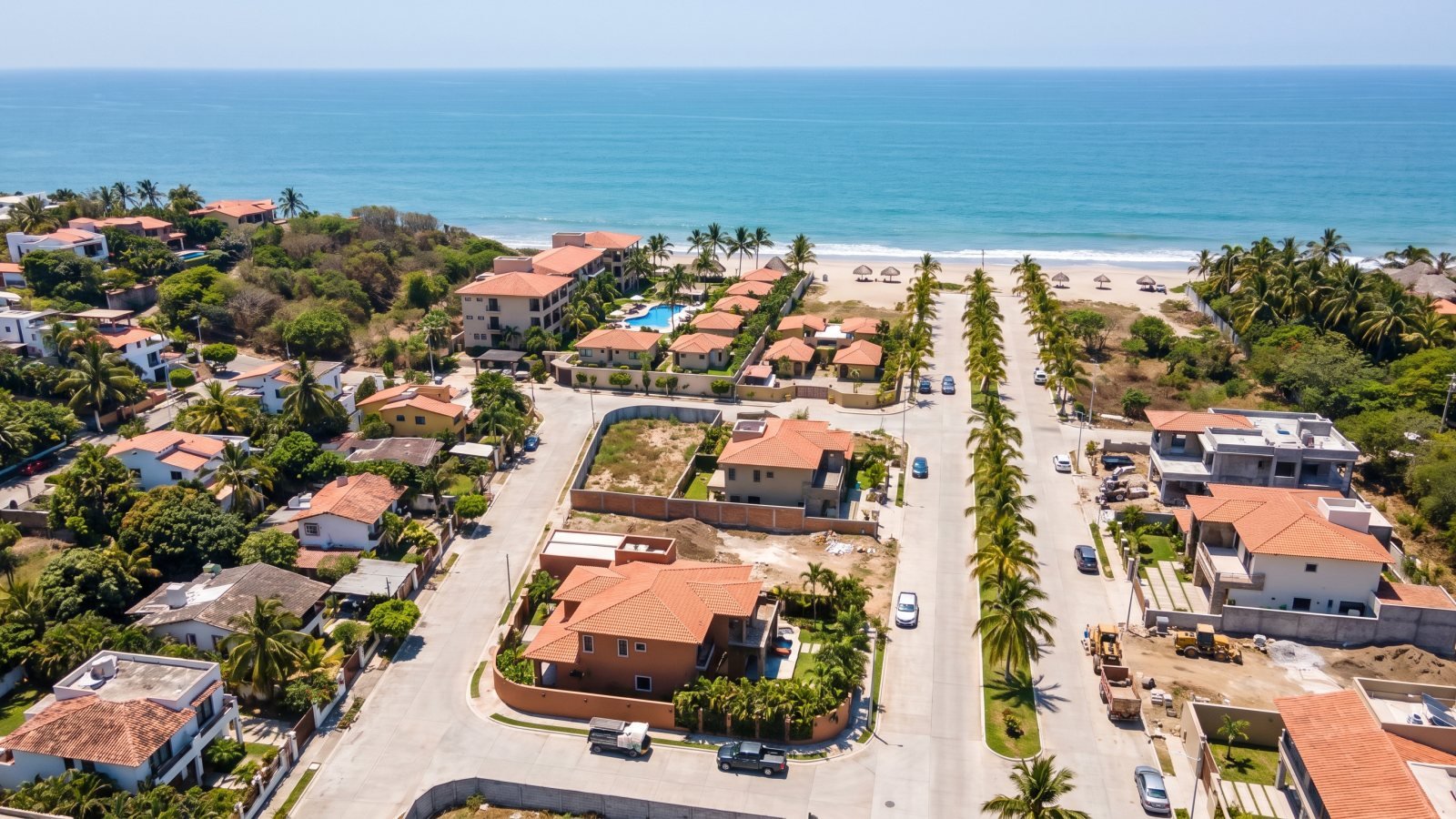 Vista aérea de una zona residencial costera en maduración en la Riviera Nayarit, con calles pavimentadas, casas nuevas y avenida de palmeras hacia el mar